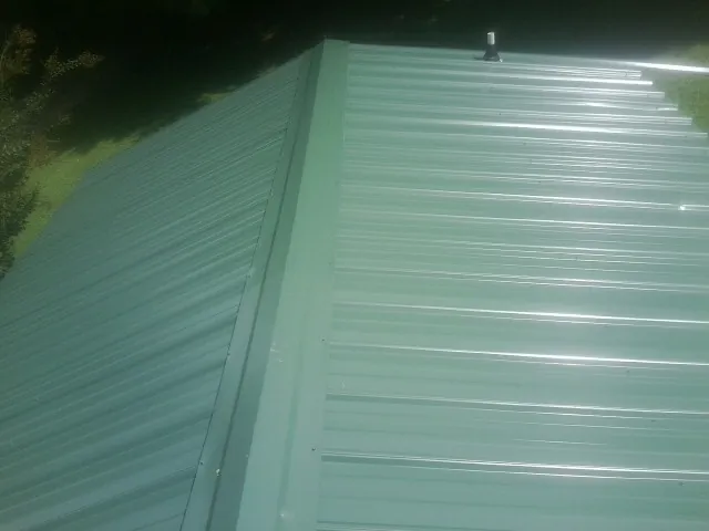 New green metal panels meeting at the ridge of a roof — Flat Roof Repair work by our crew in Crandall