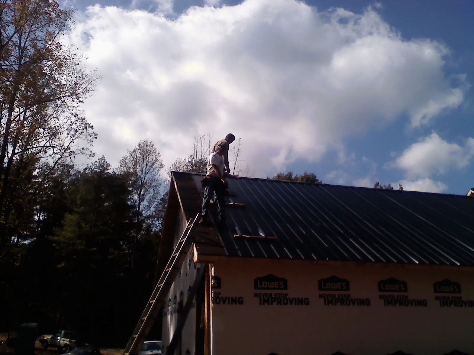 Roofer fastening dark metal panels high against a cloudy sky, from a Roof Inspection job in Crandall