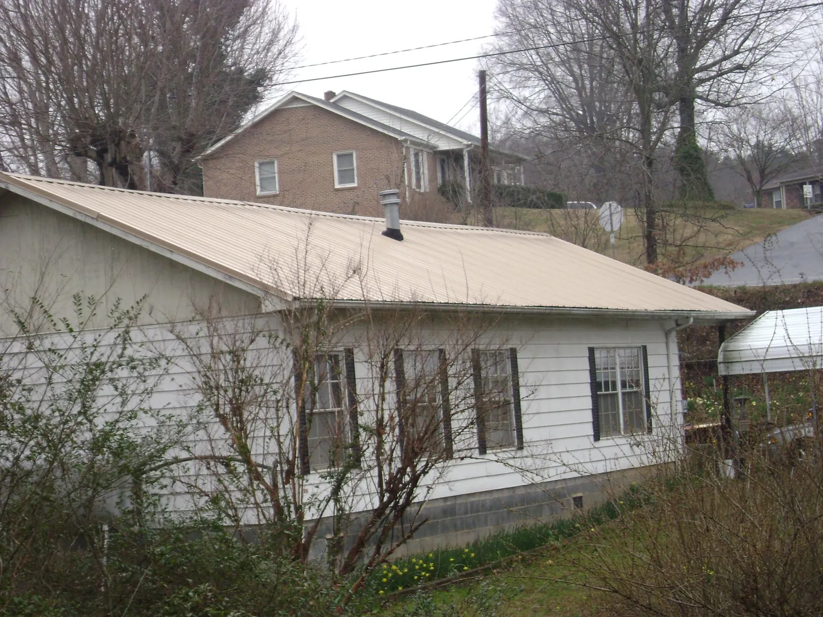 Tan metal roof on a white sided house set into a hillside — Commercial Roofing by Roofing Brothers in Crandall