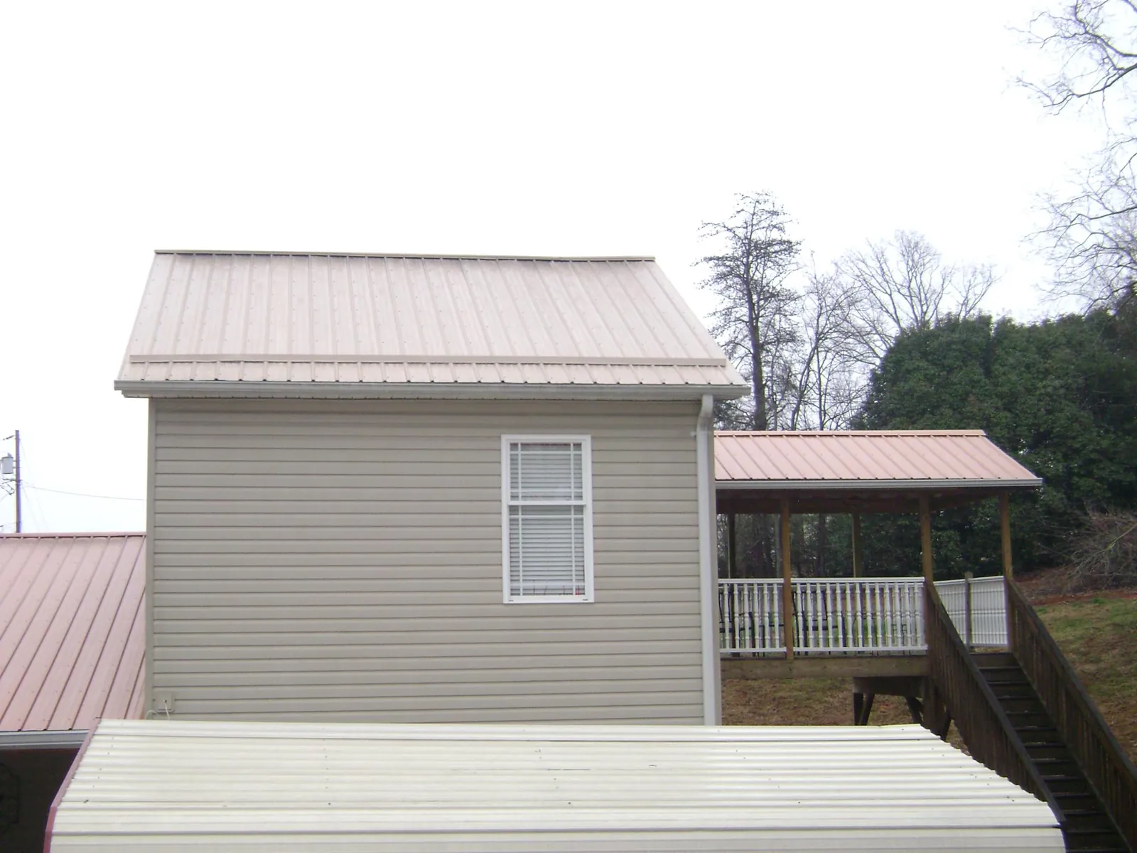 Tan metal roofs on a two story addition and attached porch, from a Roof Replacement job in Crandall